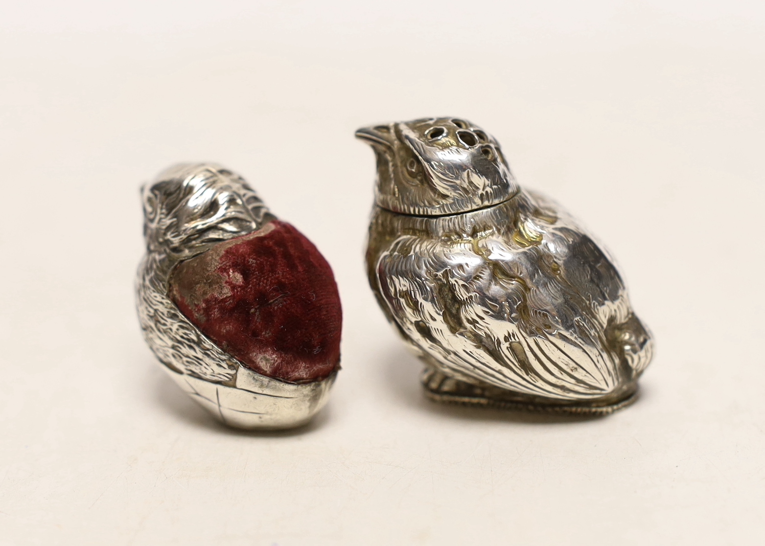 An Edwardian novelty silver pin cushion, modelled as a hatching chick, Sampson Mordan & Co, Chester, 1907, height 33mm and a late Victorian silver chick pepperette, London, 1883.